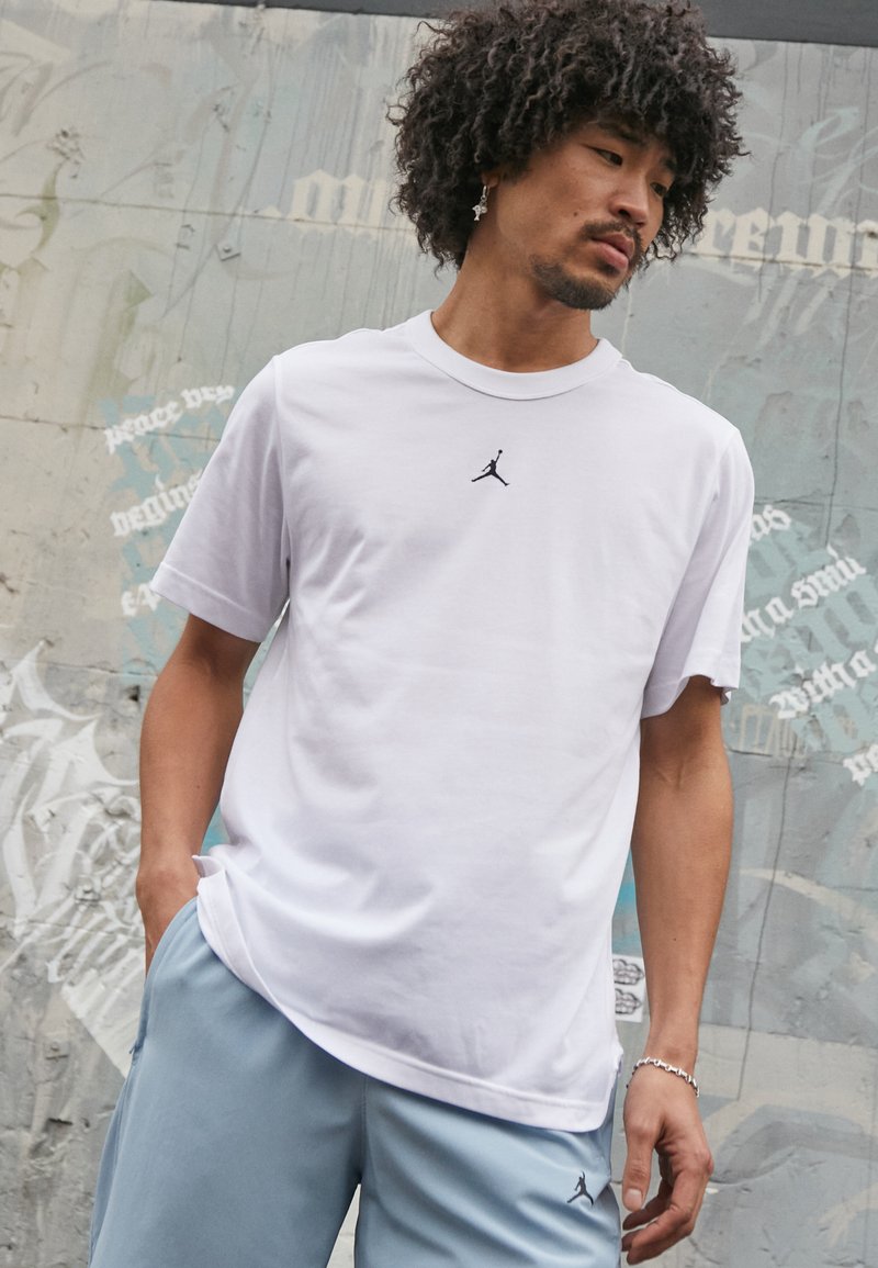Hvid bomulds T-shirt med korte ærmer, der har et sort Jordan-logo på brystet. Kombination med lyseblå sportsshorts.