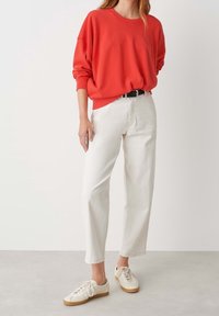 Sudadera roja de gran tamaño con mangas largas, combinada con jeans blancos de pierna recta y zapatillas blancas con suelas marrón claro.