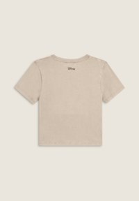 Camiseta corta de manga corta en color beige con un pequeño logo negro de Disney centrado cerca del escote trasero.