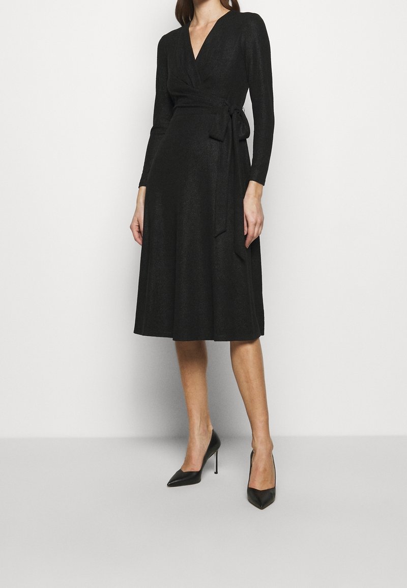 Musta kietaisumekko, jossa pitkät hihat ja V-aukko. Vyötäröllä solmittava nauha, ja helma ylettyy puoliväliin pohjetta. Sileä, teksturoitu kangas.