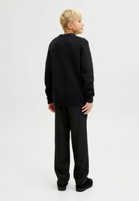 Must mustriga mustre, millel on soonilised varrukad ja alläär, mis näitab tekstiilset viimistlust. Seljas on lõdvahaisse mustad püksid ja mustad kingad.