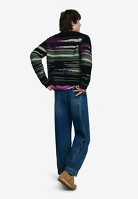 Viacfarebný pletený sveter s čiernymi, fialovými a zelenými pruhmi. Kombinovaný s voľnými modrými džínsami a hnedou obuvou. Neformálny strih a textúrovaný dizajn.