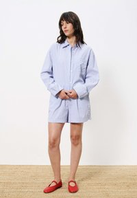 Gestreepte blauwe en witte kortemouwen shirt met een zak, gecombineerd met bijpassende shorts; de shorts hebben knopen en worden gedragen met rode ballerina's.