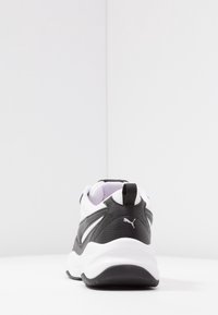 Musta-valkoinen urheilukengä, jossa on teksturoitu nahkapäällinen, pehmustettu kaulus ja valkoinen kumipohja. Takana vetokahva.