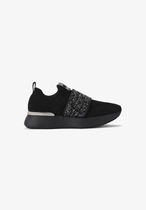Zwarte gebreide sneakers met een decoratieve zwarte en zilveren band, rubberen zool en een trekhaak aan de hiel voor gemakkelijk aan- en uittrekken. Textuurafwerking.