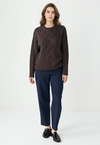 Brązowy sweter z dzianiny w wzór diamentów, okrągły dekolt i luźny krój, w połączeniu z granatowymi spodniami prostymi i czarnymi mokasynami.