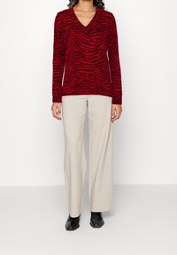 Pull rouge à col en V avec des rayures zèbre noires, en tissu doux. Associé à un pantalon beige à jambes larges et des bottines noires.