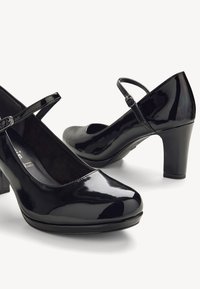 Svarta lackläderklackar med rund tå, ankelrem och medelhög klack. Slät yta med en glansig finish.
