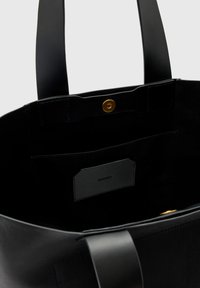 Sac fourre-tout en cuir noir à la texture lisse. Il comprend une fermeture à pression dorée, une poche intérieure et des poignées plates pour un transport facile.