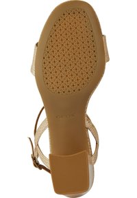 Sandale beige avec une semelle extérieure en caoutchouc perforé et des fines lanières. Dotée d'une tige texturée avec une boucle à la cheville pour un maintien sécurisé. Marquage Geox visible.