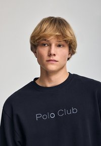Sudadera de color náutico hecha de algodón, con cuello redondo y hombros caídos. Logo de "Polo Club" impreso en gris en el pecho.