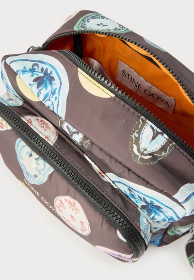 Υφασμάτινη τσάντα χιαστί με μαύρο φερμουάρ, πολύχρωμα κυκλικά λουλουδένια μοτίβα και φωτεινή πορτοκαλί εσωτερική επένδυση με την ετικέτα "STINE GOYA".