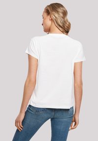 White cotton T-shirt with short sleeves, round neckline, relaxed fit, and visible stitching details, worn with blue jeans.