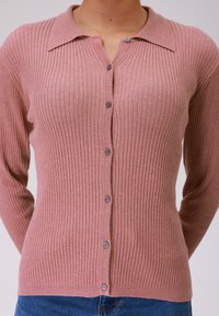 Rausvas pūkuotas megztinis su apykakle, ilgomis rankovėmis ir penkiomis pilkomis mygtukais priekyje. Minkšta tekstūra be matomų raštų.