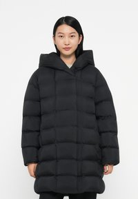 Mustahi puffer-takkia, jossa on tikattu muotoilu, suuri huppu ja pitk�ät hihat. Sileä pinta, lantiota alempi pituus, minimalistinen tyyli.