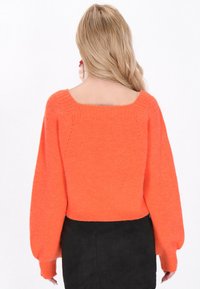 Pull court en tricot orange vif, avec des manches larges et un décolleté carré, possédant une texture côtelée et une finition soignée au niveau de l'ourlet.