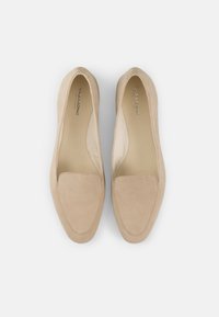 Mocasines de ante beige con punta redonda, suela plana y panel lateral expuesto. El diseño simple presenta un acento cosido en la parte superior.