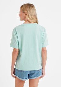 Woman facing away wearing a light blue oversized T-shirt and rolled-up denim shorts against a plain white background.