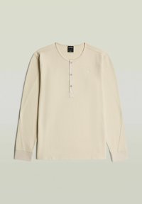 Beige langærmet vaffelstrikket skjorte med rund hals, tre-knaps åbning, ribstrikkede manchetter og lille logo på venstre bryst.