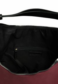 Burgundyröd handväska med invändig svart tygfoder, en dragkedjeficka och en slät dragkedjeslutning längs den övre kanten.