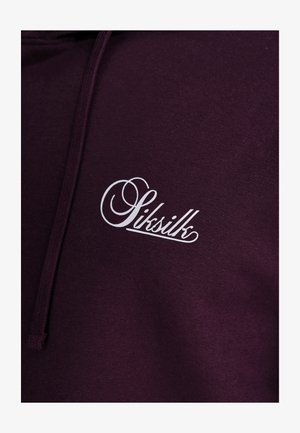 Dark purple hoodie featuring a white script logo with a looping design. Material appears soft with a textured finish and adjustable drawstring.