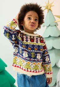 Maglione di maglia con base blu e motivi festivi, inclusi pupazzi di neve e alberi, scollo color crema e orlo a coste. Indossato con pantaloncini di denim.