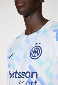 Mies, joka pukeutuu valkoiseen ja vaaleansiniseen kuvioituun urheilu-paidan, jossa on Inter Milanin logo ja Betsson Sportin sponsorin nimi.