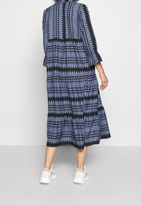 Robe maxi noire et bleue à motifs avec manches trois-quarts, design à volants en plusieurs couches et ourlet à volants, associée à des baskets blanches.