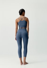Niebieski zestaw sportowy z prążkowanym crop topem z krzyżującymi się ramiączkami oraz legginsami z wysokim stanem, gładka tekstura, dopasowany fason.