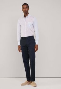 Camicia a righe rossa e blu, pantaloni navy e scarpe slip-on beige. Presenta una tasca sul petto e maniche lunghe.