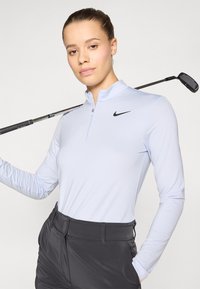 Maglia da golf azzurro chiaro a maniche lunghe con collo a mezza zip e righe orizzontali; presenta un logo Nike nero sul petto. Pantaloni da golf neri.