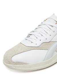 Baltos sportbačiai su minkštu pilkos zomšo priekiu, tekstūruota odine viršutine dalimi, baltais raišteliais ir šviesiu guminiai padu su dėmėtais akcentais.