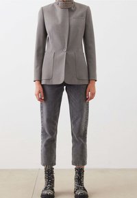 Šedé sako s vysokým límcem, zapínáním na knoflíky vpředu a dvěma kapsami, doplněné šedými džínami z denimu a kotníkovými botami se zvířecím potiskem.