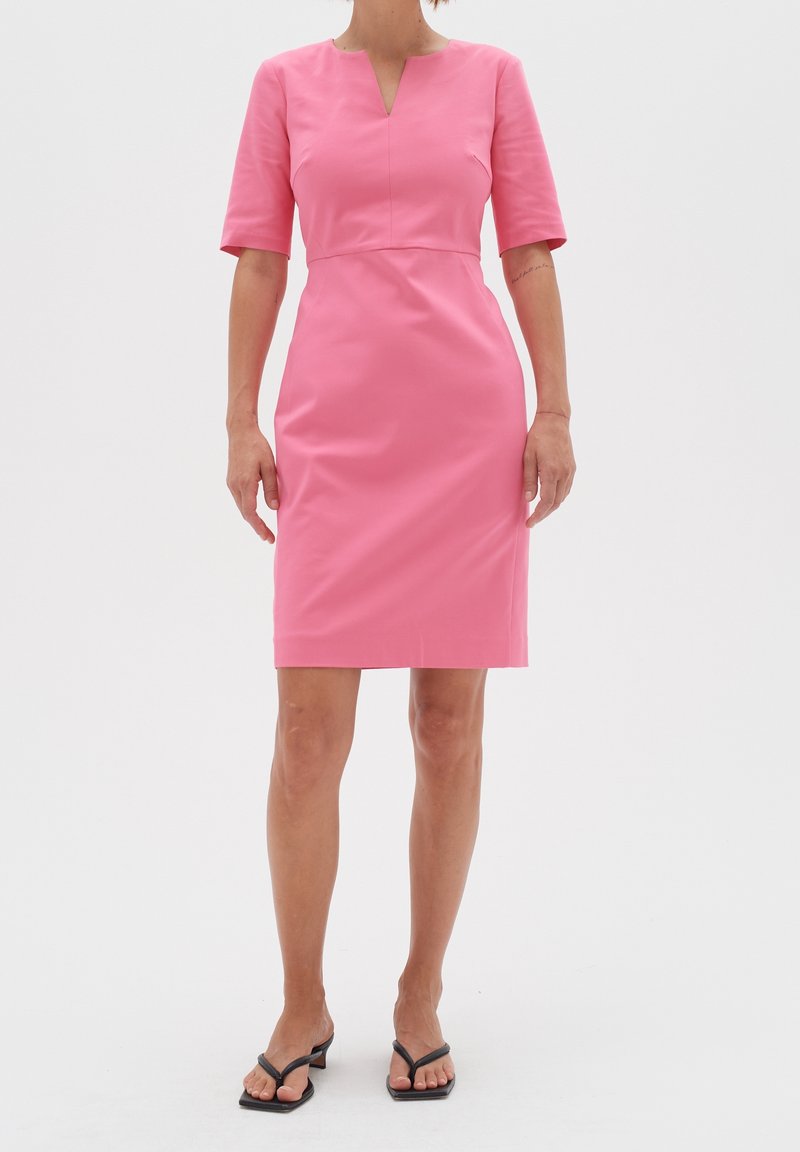 Rosa figurnära klänning med V-ringning, korta ärmar och knälång fåll. Tillverkad av slät tyg, med en enkel design utan mönster.