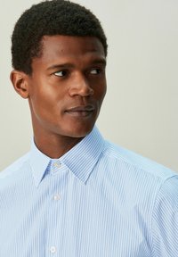 Camisa de vestir a rayas azul claro hecha de algodón, con cuello puntiagudo y cierre de botones, de textura suave y corte entallado.