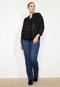 Black lace shirt with floral texture, loose fit, button-up design. Paired with dark blue flared jeans and black ankle boots.