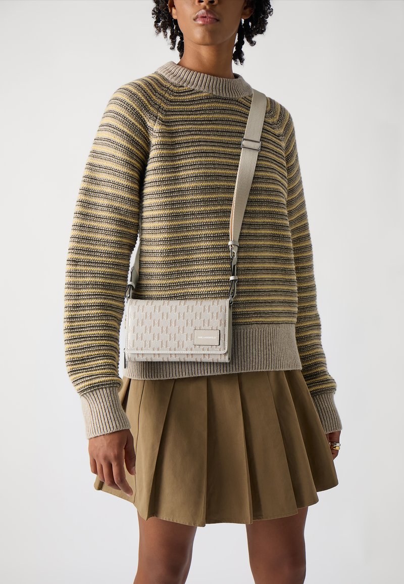 Crossbody bag in textured cream fabric featuring a subtle geometric pattern and a metal logo. Adjustable strap in light beige.