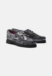 Metallic schwarze Bootsschuhe mit grauen Schnürsenkeln, strukturiertem Obermaterial und dickem schwarzen Gummisohle, die ein Musterprofil für Grip aufweist.