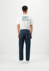White graphic t-shirt featuring a mountain design and "Timberland" text on the back, paired with loose-fitting blue denim jeans and white sneakers.