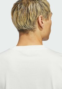 Biela bavlnená tričko s okrúhlym výstrihom, s hladkou textúrou a jednoduchým designom. Obraz ukazuje zadný pohľad.