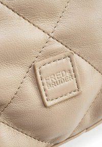 Beige leren handtas met gewatteerde textuur en contrasterende stiksels. Heeft een vierkante leren label met de opdruk "FREDS BRUDER."