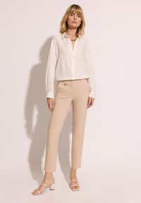 Lekka biała lniana koszula zapinana na guziki w połączeniu z beżowymi spodniami o dopasowanym kroju oraz sandałami na słupku z paskami; gładkie faktury i czyste linie.