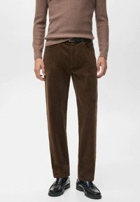 Pantalones de pana marrón con corte recto, textura acanalada, bolsillos frontales y una cinturilla suave, combinados con zapatos negros.