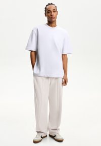 Light gray oversized t-shirt, short sleeves, crew neck, paired with loose, light beige trousers. White sneakers with black swoosh detailing.