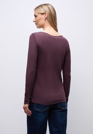 T-shirt à manches longues en mauve profond, en tissu doux, avec un col rond et une coupe ajustée. Associé à un jean bleu foncé, montrant une vue arrière élégante.
