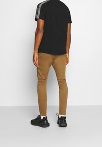 Black short-sleeve shirt with gray side stripes, paired with tan slim-fit pants. Black sneakers with textured sole and white socks.