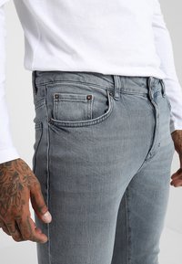Vaqueros de denim gris claro con un corte ajustado, diseño de cinco bolsillos, desvanecimiento sutil y detalles en tono de cobre.