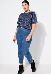 Top blu con motivo floreale e maniche corte; jeans in denim alta vita con decorazioni in perle; stivali neri con lacci.