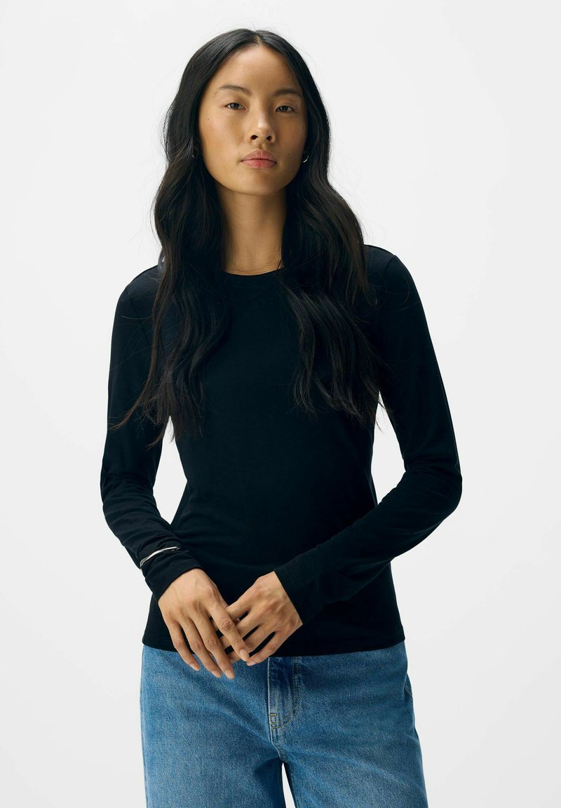 Sort langærmet skjorte med rund halsudskæring, lavet af blødt stof, parret med lyseblå denimjeans. Enkel design med minimal detaljering.
