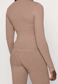 Prążkowany top z długim rękawem w jasnobrązowym materiale, dopasowany krój, z okrągłym dekoltem i bezszwową konstrukcją, zestawiony z pasującymi prążkowanymi spodniami.